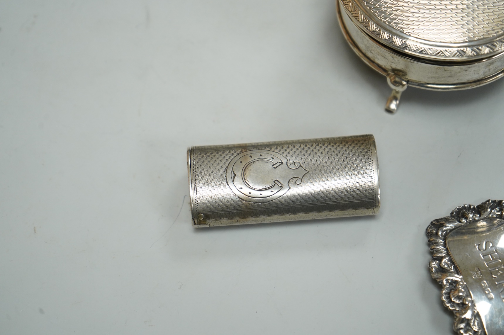 A George V silver mounted circular trinket box by Horton & Allday, Birmingham, 1916, diameter 75mm, together with a 19th century German? white metal vesta case and a modern silver wine label.